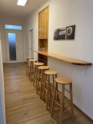 A hallway with wooden flooring, a bar area with stools, and a coffee-themed wall decoration. - Room Da Tea – Rooms with Shared Bathroom, Mountain View, Wi-Fi and Air Conditioning (Olzai)