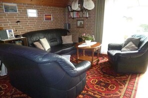 A living room with a brick wall, leather sofas, a coffee table, and a bookshelf. - Holiday home with 2 bedrooms (Wurster Nordseeküste)