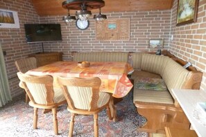 A dining area with a brick wall, a television mounted above a table, and a clock. - Holiday home with 2 bedrooms (Wurster Nordseeküste)