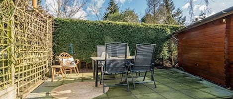 An outdoor patio with a table and chairs, surrounded by a wooden fence and a hedge.