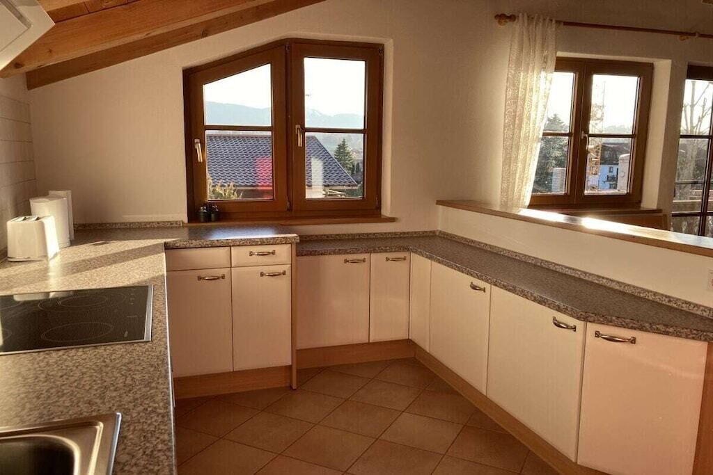 Eine Küche mit eingebautem Herd, weißen Schränken und einem Fenster mit Blick auf ein Haus und Berge.