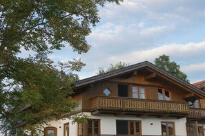 Une maison en bois à deux étages, dotée d’un balcon, de grandes fenêtres et d’une façade blanche.
