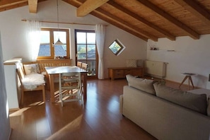 A spacious room with a wooden ceiling, a dining table with chairs, a sofa, and a small window. - Holiday apartment with 2 bedrooms (Bad Bayersoien)