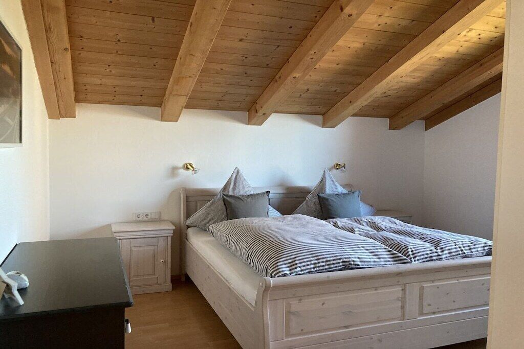 Un dormitorio con techo de madera, una cama con almohadas, una mesita de noche y un tocador.