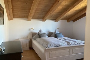 A bedroom with a wooden ceiling, a bed with pillows, a bedside table, and a nightstand. - Holiday apartment with 2 bedrooms (Bad Bayersoien)