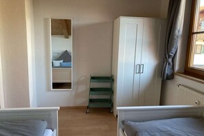 Une chambre avec deux lits, une armoire, un chariot vert et une fenêtre avec des rideaux.