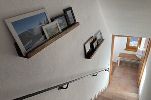 Un escalier avec une rampe, une étagère fixée au mur ornée de tableaux encadrés et une fenêtre donnant sur l’extérieur.