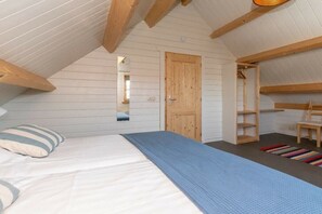 Ein Schlafzimmer mit einem Bett, einer Holztür, einem Spiegel und einem kleinen Fenster.