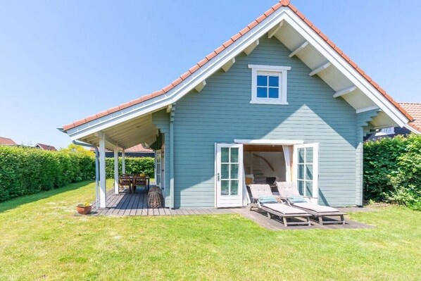 Einbungalow mit überdachter Veranda, einer kleinen angebauten Garage und einem Rasen mit Gartenmöbeln.