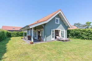 Ein eingeschossiges Haus mit geneigtem Dach, einer überdachten Veranda und einer kleinen Terrasse.