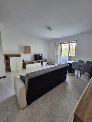 A modern living room with a sofa, a TV, and a dining area with chairs. - Vrbo Property (Roma)
