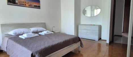 Une chambre à coucher comprenant un lit, une table de chevet, une commode, un miroir et un tableau représentant le Colisée.