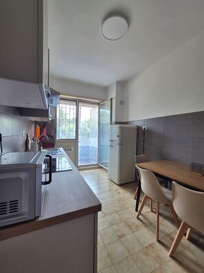A modern kitchen with a built-in microwave, a refrigerator, and a dining area with a wooden table and chairs. - Vrbo Property (Roma)