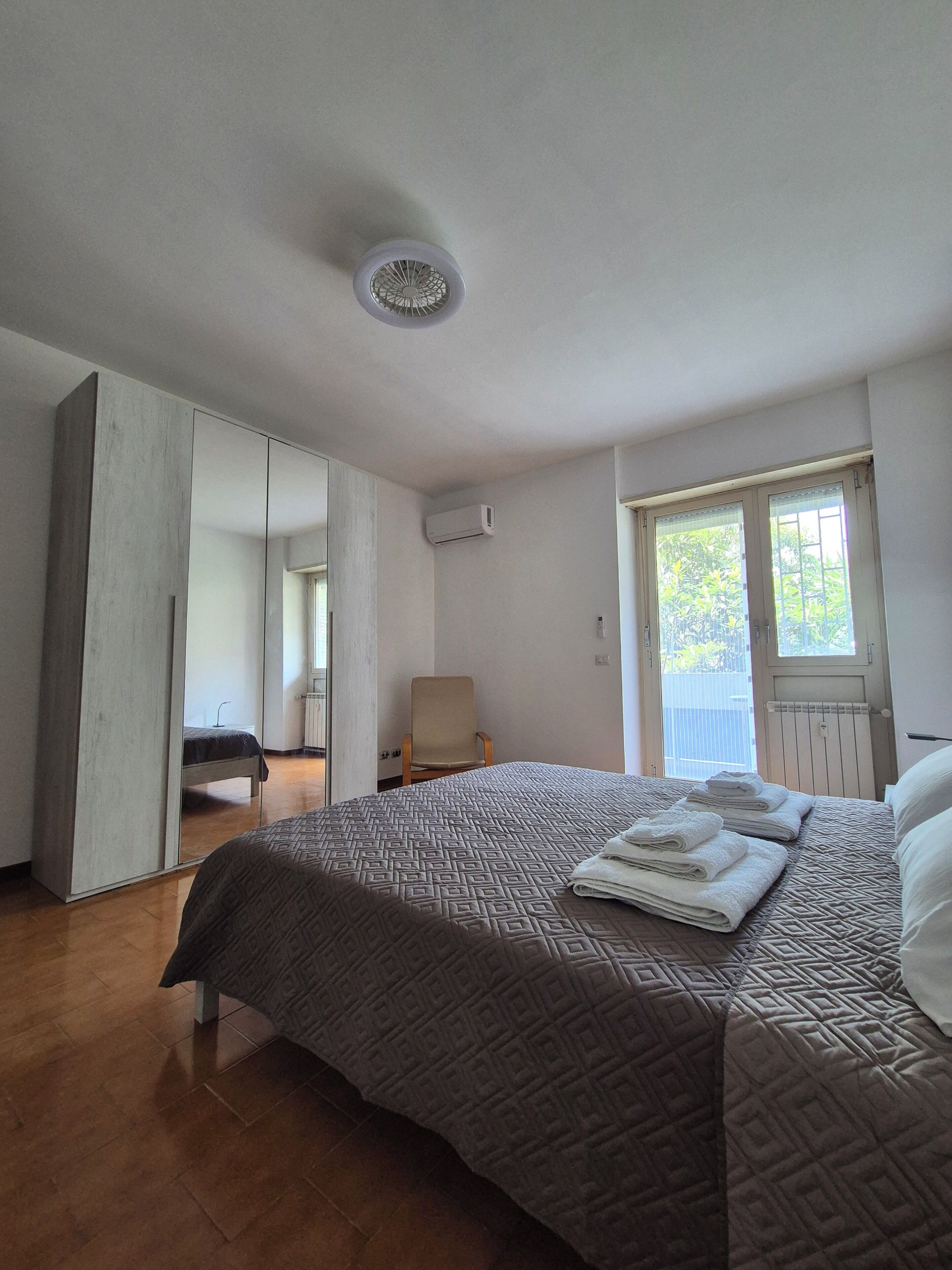 A bedroom with a large bed, a chair, a wardrobe, and a window with a view.