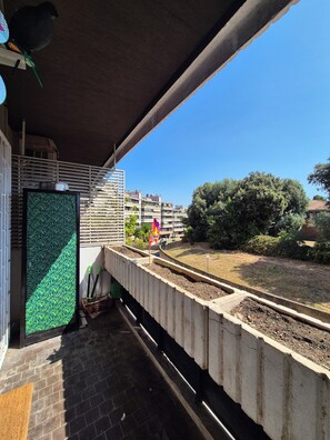 Ein Balkon mit Blick auf eine Wohngegend, einem Betonpflanzgefäß und einem Metallgeländer.