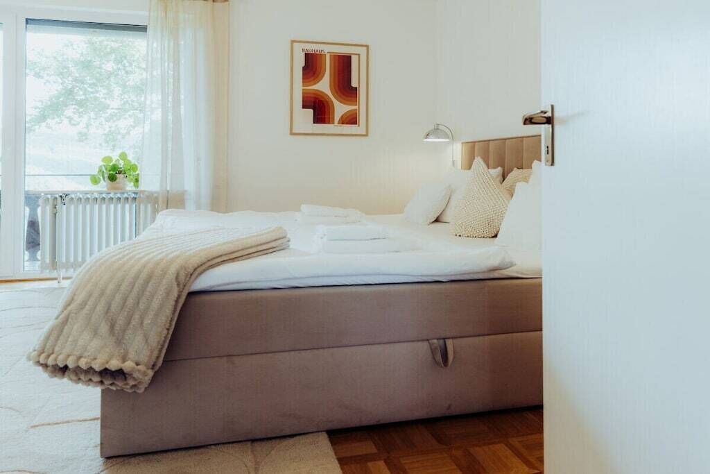 Een slaapkamer met een bed, een radiator, een raam met gordijnen en een wandlamp.