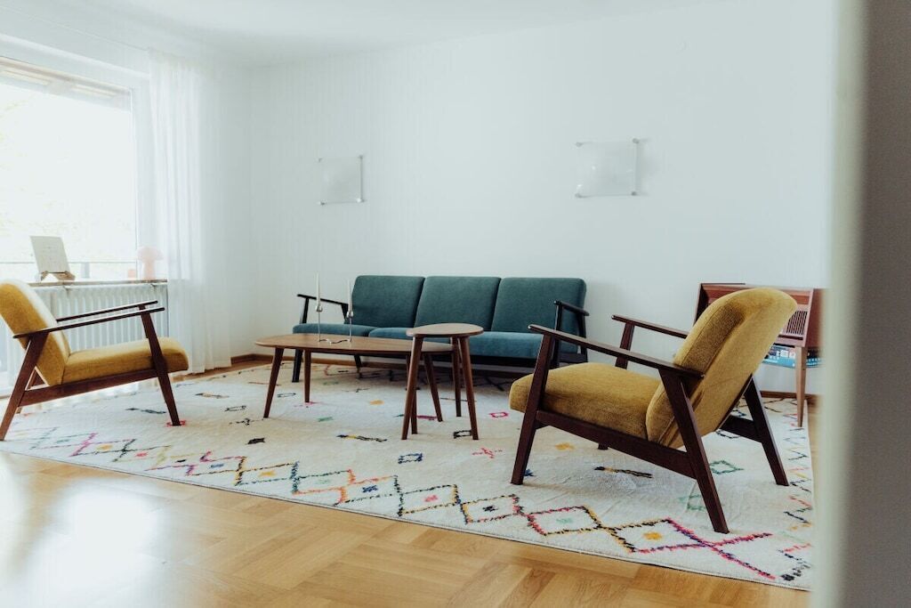 Una sala de estar con un sofá, dos sillones, una mesa de centro y un tapete estampado.