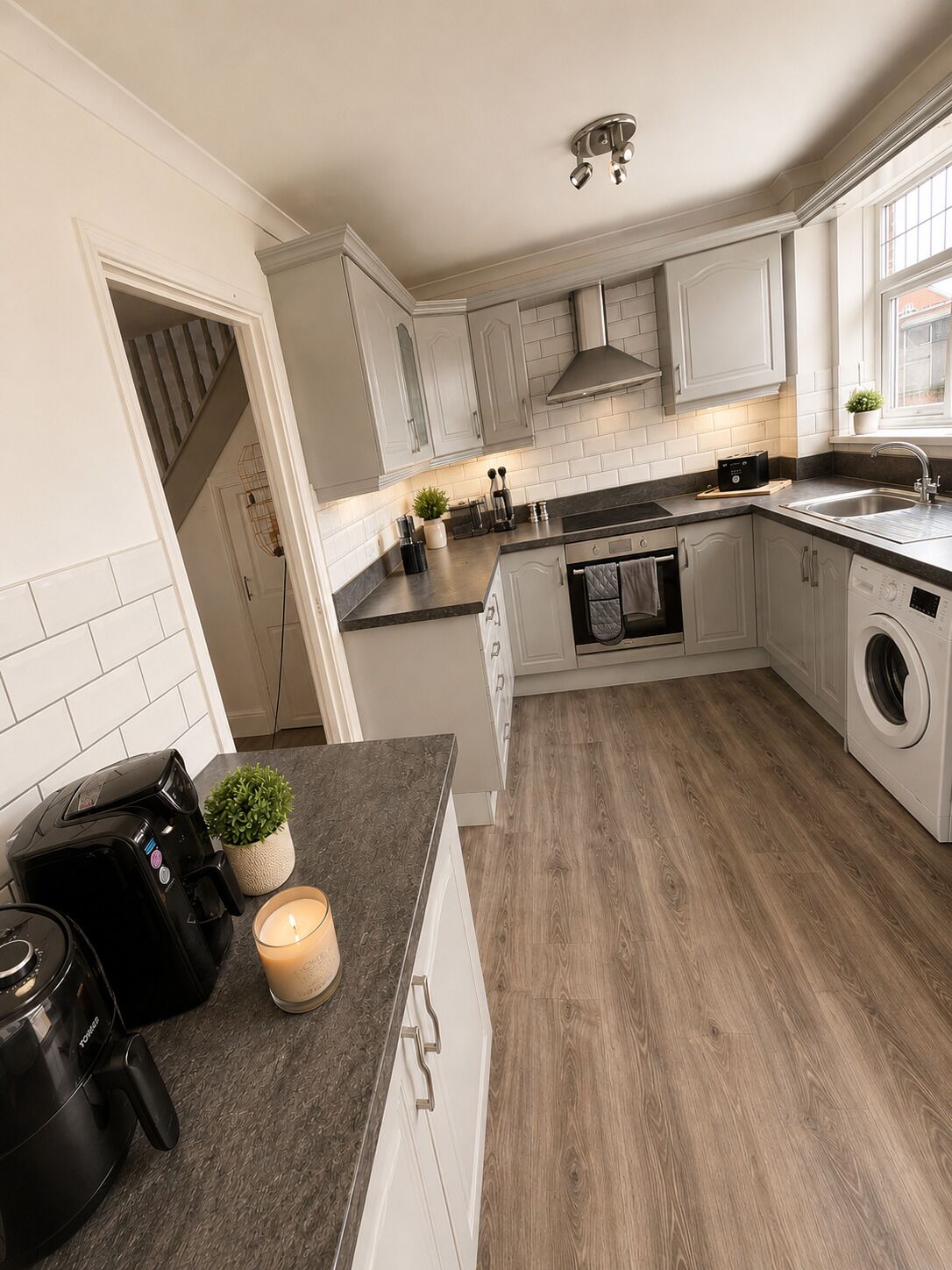 A modern kitchen with white cabinetry, a built-in oven, a washing machine, and a coffee maker on the counter.