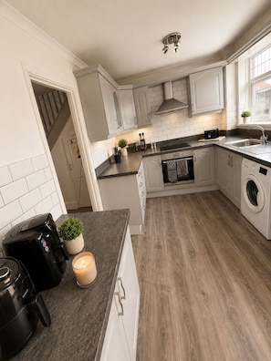 A modern kitchen with white cabinetry, a built-in oven, a washing machine, and a coffee maker on the counter. - Ellington Escape lovely 3 bedroom house (Morpeth)