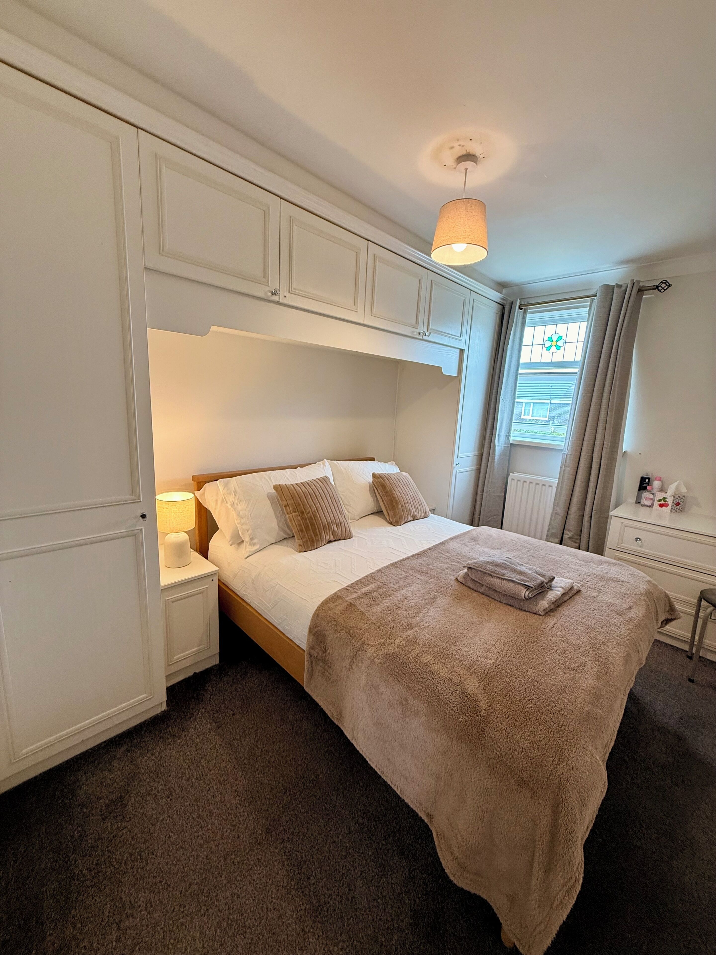 A bedroom with a bed, nightstands, a lamp, a window with curtains, and a radiator.