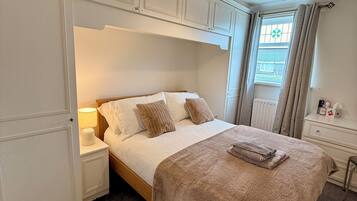 A bedroom with a bed, nightstands, a lamp, a window with curtains, and a radiator.