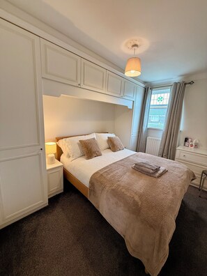 A bedroom with a bed, nightstands, a lamp, a window with curtains, and a radiator.