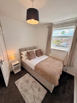 A bedroom with a bed, bedside lamp, window, and a view of the outside. - Ellington Escape lovely 3 bedroom house (Morpeth)