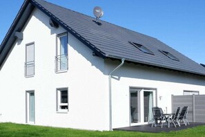 A modern two-story house with a sloped roof, satellite dish, and a patio with outdoor furniture. - Holiday home in Burhave with swimming pool (Burhave)