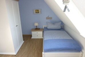 A bedroom with a single bed, a nightstand, a lamp, and a wall-mounted shelf with a picture frame and a word sign. - Holiday apartment with 2 bedrooms (Kappeln)