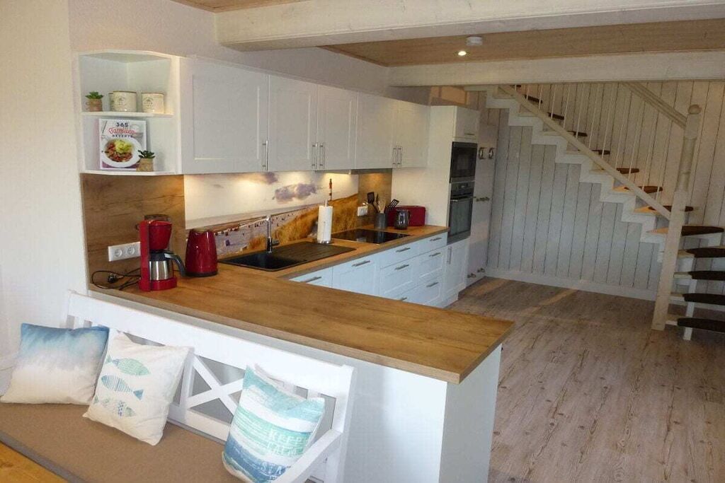 Una cucina moderna con mobili bianchi, un piano di lavoro in legno e un piano cottura integrato.