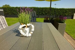 Un patio con un'aiuola a forma di cuore realizzata con pietre, una pianta in vaso con fiori viola e un cuscino a righe.