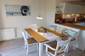 A dining area with a wooden table, white chairs, and a painting of a dog on the wall. - Holiday apartment with 2 bedrooms (Kappeln)