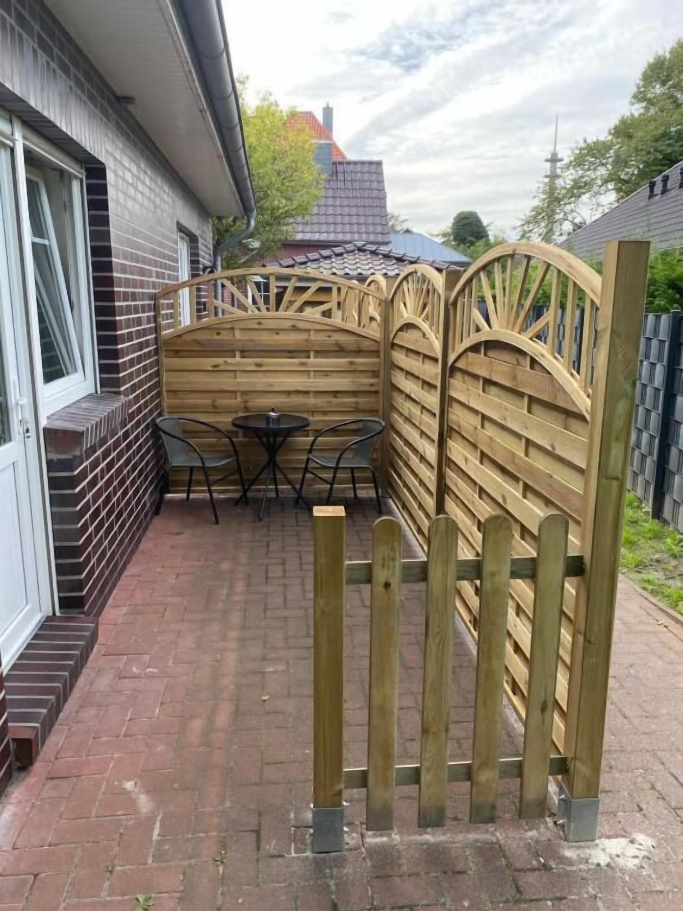Eine Terrasse aus Ziegelsteinen mit einem Holzzaun und einem Tisch mit Stühlen.