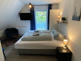 A bedroom with a bed, bedside lamps, a TV, and a window with curtains.