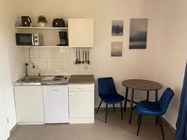 A compact kitchen with a microwave, coffee maker, and utensils on the wall. There is a small dining area with two chairs and a table.