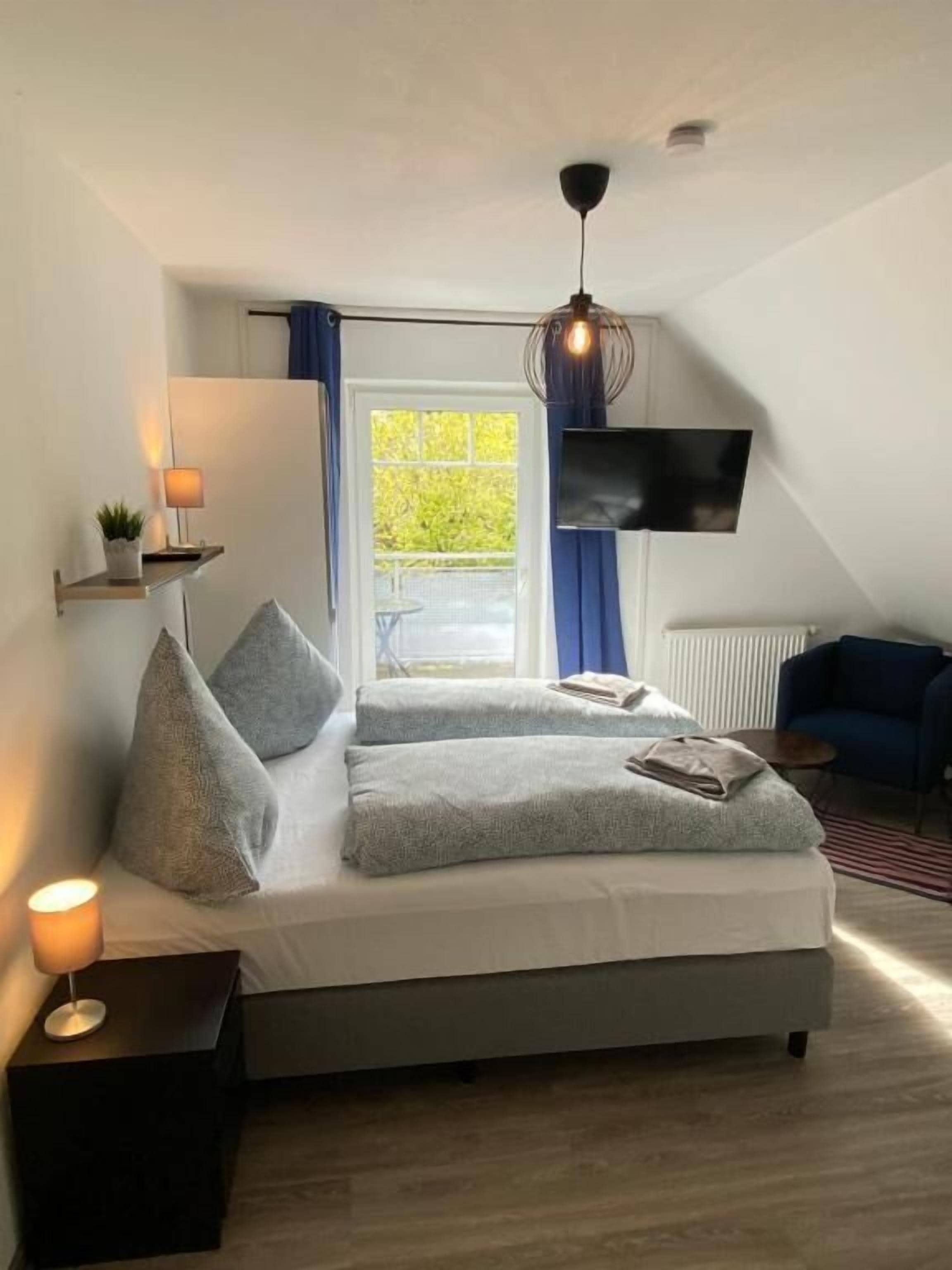 A modern bedroom with a bed, bedside lamps, a TV, and a window with curtains.