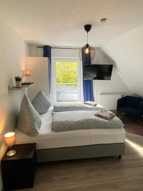 A modern bedroom with a bed, bedside lamps, a TV, and a window with curtains. - Haus Osterstraße (Norden)