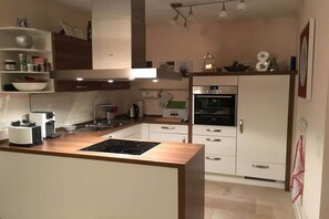 A modern kitchen with a central island, built-in oven, and white cabinetry. - Holiday home with 2 bedrooms (Kronsgaard)