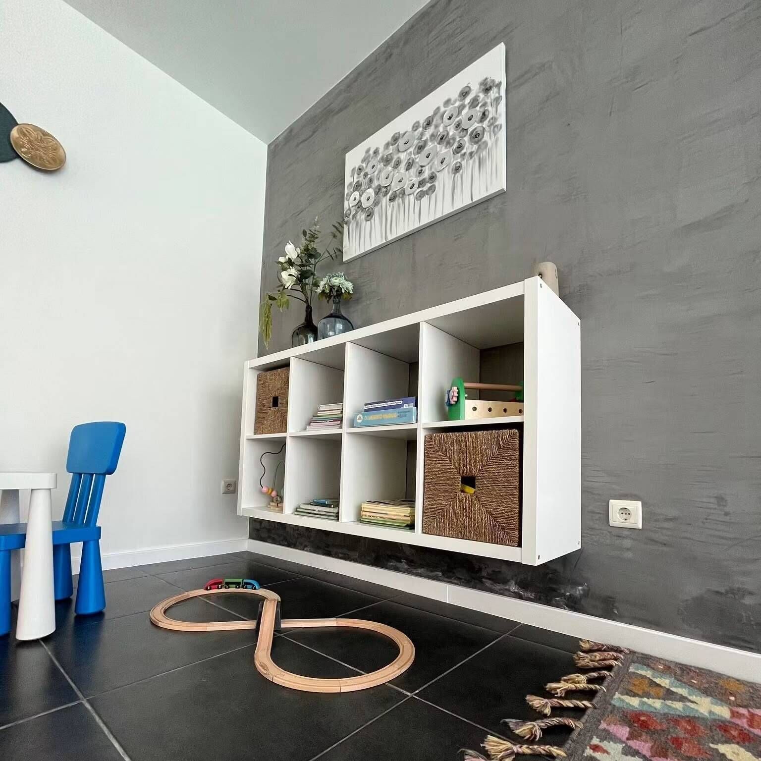 Un salón moderno con una estantería empotrada blanca, un sillón azul y un suelo de baldosas negras.