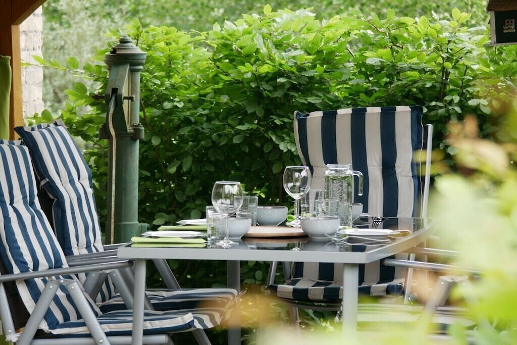 An outdoor dining area with striped chairs and a table set for two, surrounded by lush greenery.