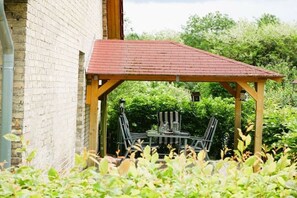 Een overdekt terras met een tafel en stoelen, omringd door groen.