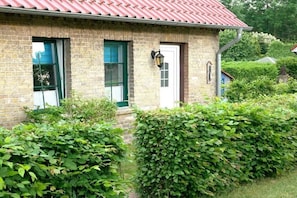Een bakstenen gebouw met een rood dak, een witte deur en een raam met een groene omlijsting.