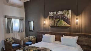 Habitación de hotel con una cama grande, dos sillones de mimbre con cojines azules, un cuadro de un leopardo en un árbol, y una lámpara fijada a la pared.