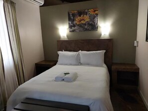 A hotel room with a bed, two bedside tables, a headboard, and a wall-mounted artwork. - Kruger Whispering Waters (Hazyview)