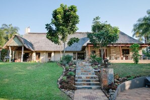 A house with a thatched roof, a stone staircase, and a well-maintained lawn. - Kruger Whispering Waters (Hazyview)