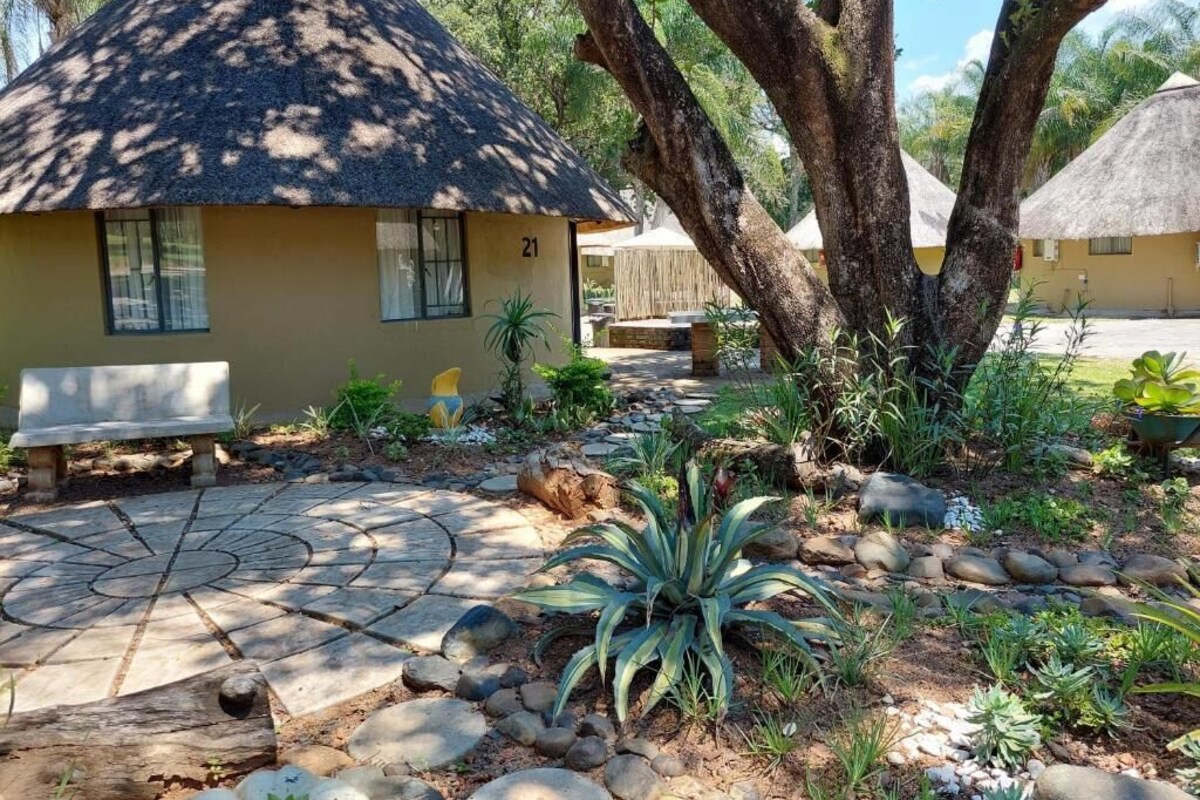 A thatched-roof building with a number '21' on the side, surrounded by a garden with various plants and a stone pathway.