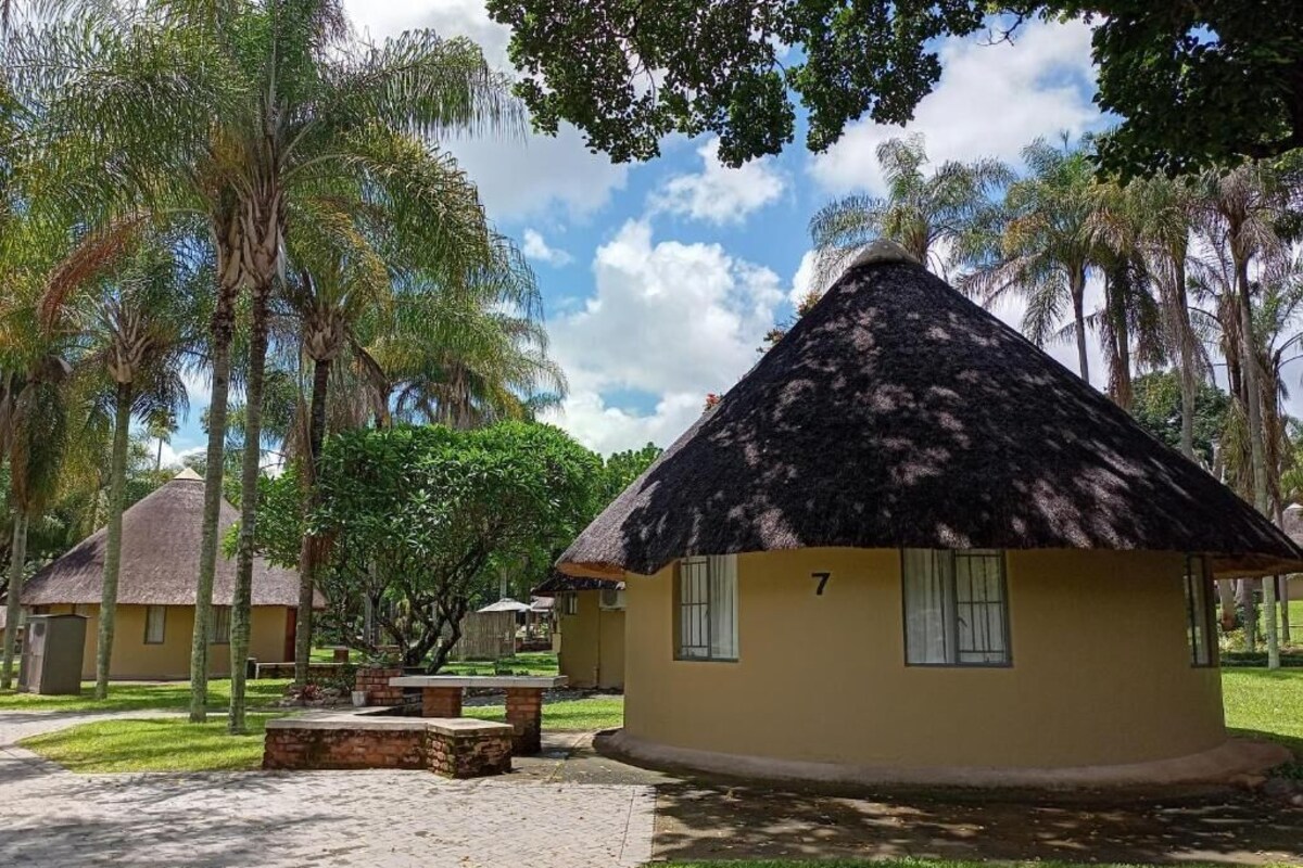 A thatched-roof building with a number '7' on its side, surrounded by greenery and other similar structures.