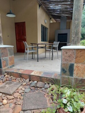 An outdoor patio area with a table and chairs, a stone pathway, and a door. - Kruger Whispering Waters (Hazyview)