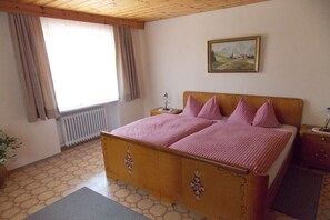 Ein Schlafzimmer mit einem hölzernen Bett, einem Nachttisch, einem Heizkörper, einem Fenster mit Vorhängen und einem Gemälde an der Wand.