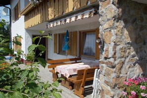 Ein Steinhaus mit einem hölzernen Balkon, einem Tisch mit Tischdecke und Topfpflanzen.